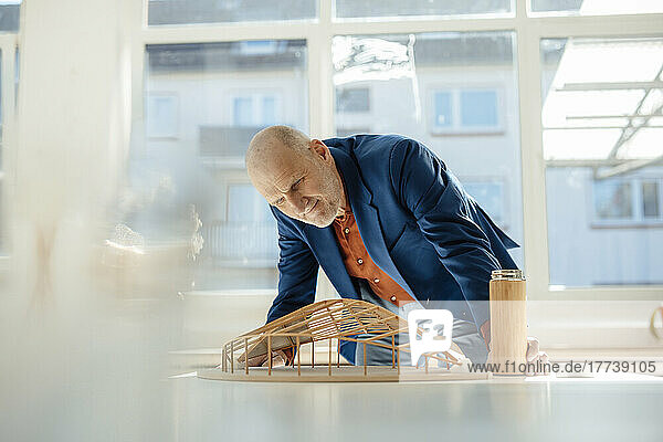 Senior architect holding water bottle analyzing leaf shape model on desk