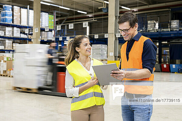 Happy worker discussing over tablet PC with young colleague in warehouse