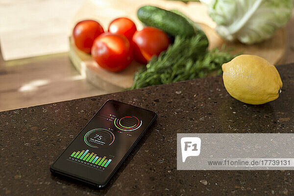 Smartphone with charts on kitchen counter next to vegetables