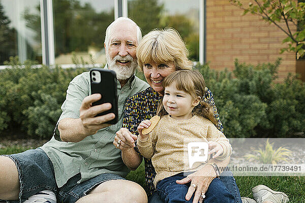 Smiling grandparents taking selfie with granddaughter (4-5) on back yard