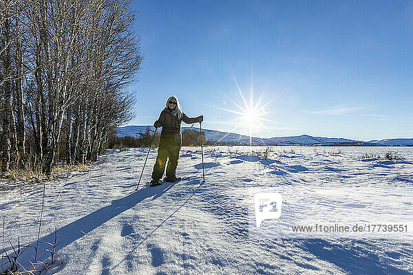 USA  Idaho  Bellevue  Senior blonde woman snow shoeing in snow covered landscape on sunny day
