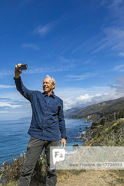 USA  California  Big Sur  Smiling senior man taking selfie at Big Sur coast