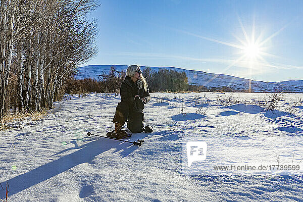 USA  Idaho  Bellevue  Senior blonde woman with snow shoes looking at snow covered landscape on sunny day