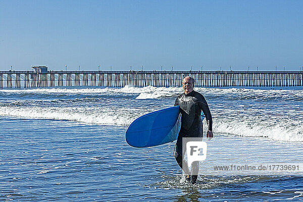 USA  California  Oceanside  Senior surfer carrying surfboard