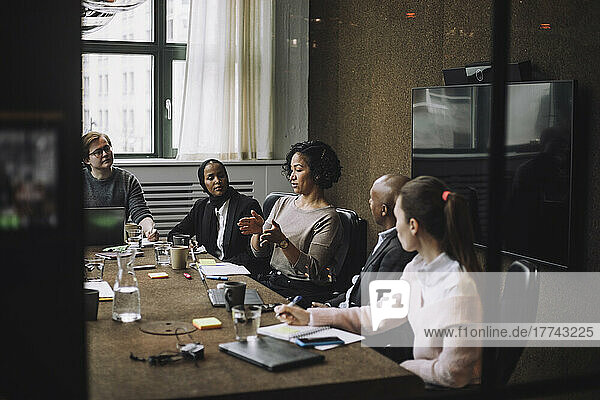 Männliche und weibliche Kollegen betrachten eine Geschäftsfrau  die am Konferenztisch sitzend Ideen austauscht  während sie gestikulieren