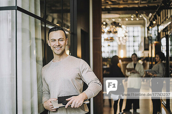 Porträt eines lächelnden reifen männlichen Unternehmers  der mit einem Laptop im Büro steht