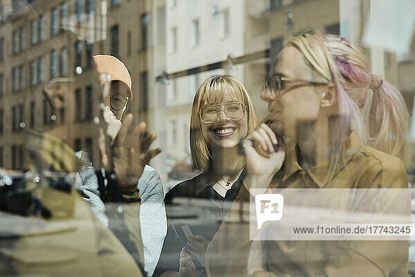 Smiling colleagues discussing together seen through glass wall of tech start-up office