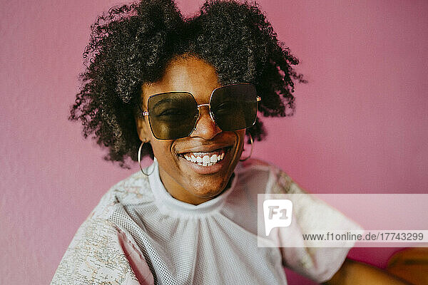 Happy hipster woman wearing sunglasses against pink wall at home