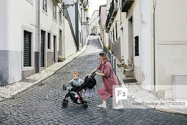 Mutter geht mit männlichem Kleinkind im Kinderwagen auf der Straße spazieren
