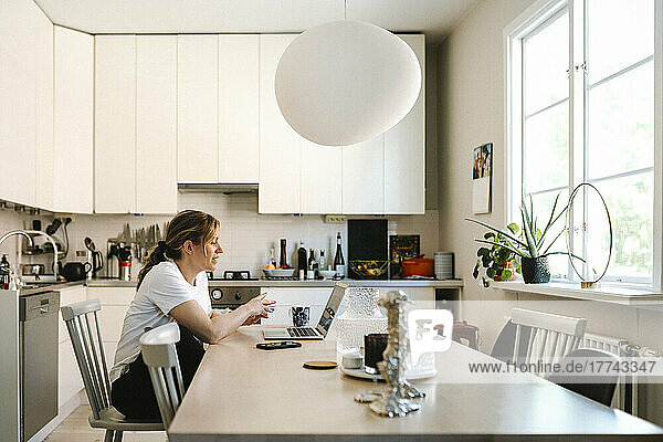 Weibliche Freiberuflerin diskutiert per Videoanruf über Laptop in der Küche zu Hause
