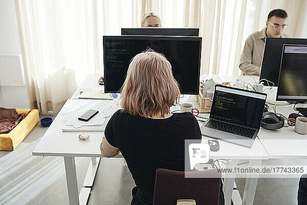 Rückansicht einer Geschäftsfrau  die an einem Computer arbeitet  während sie am Schreibtisch im Büro sitzt