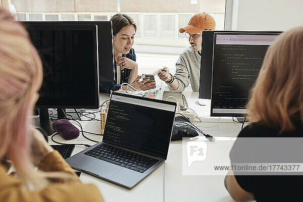 Männliche und weibliche Unternehmer  die sich bei der Arbeit im Büro über ihr Smartphone unterhalten