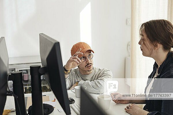 Male programmer gesturing while discussing with female colleague at tech start-up office