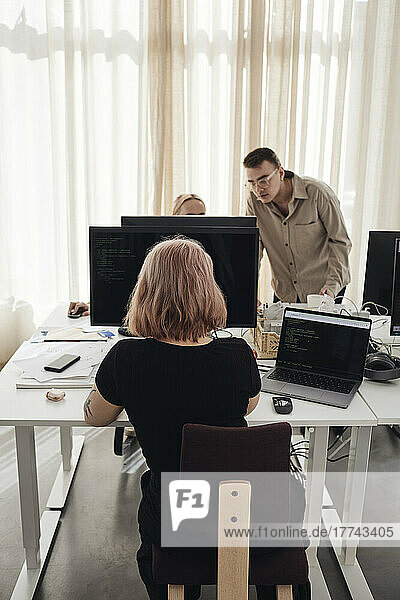 Businesswoman using computer at desk while colleagues discussing in office