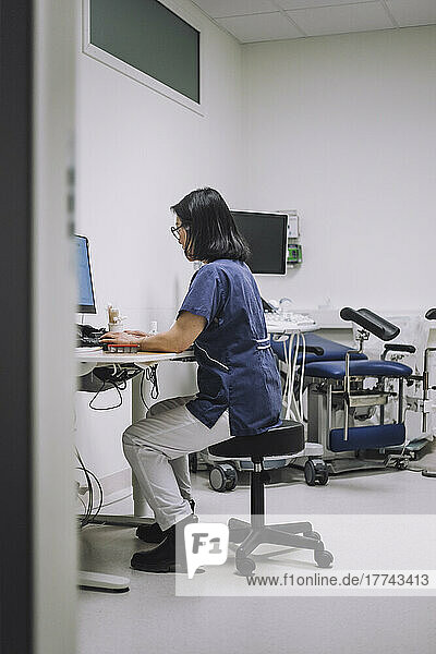 Weiblicher Gesundheitsexperte in voller Länge am Computer sitzend am Schreibtisch in einer medizinischen Klinik