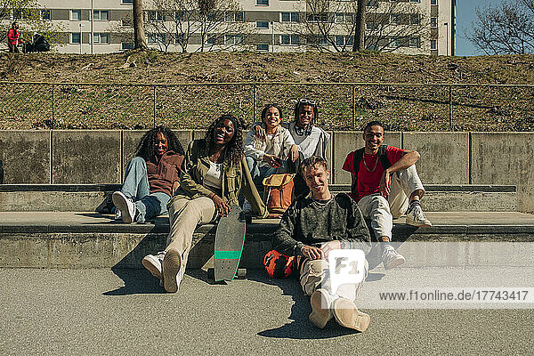 Lächelnd multirassische männliche und weibliche Freunde sitzen zusammen im Park an einem sonnigen Tag
