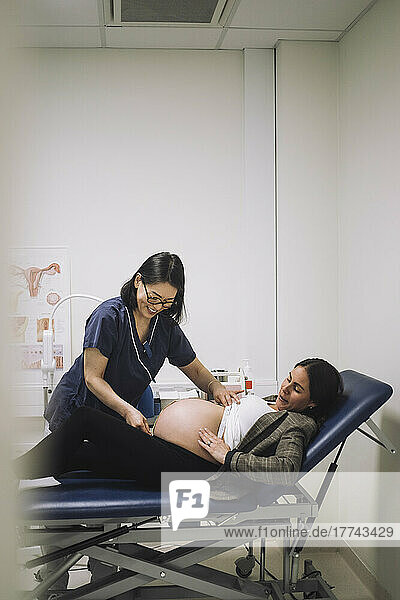 Lächelnder Gynäkologe misst den Unterleib einer schwangeren Frau  die auf einer Trage im Krankenhaus liegt