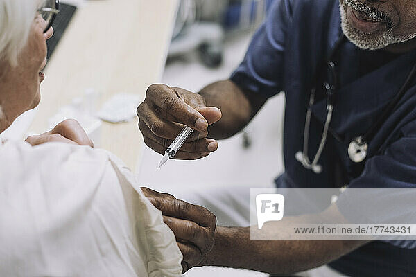 Male doctor injecting senior female patient in medical clinic
