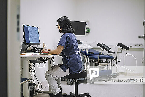 Seitenansicht einer Ärztin  die einen Desktop-PC am Schreibtisch in einer medizinischen Klinik benutzt