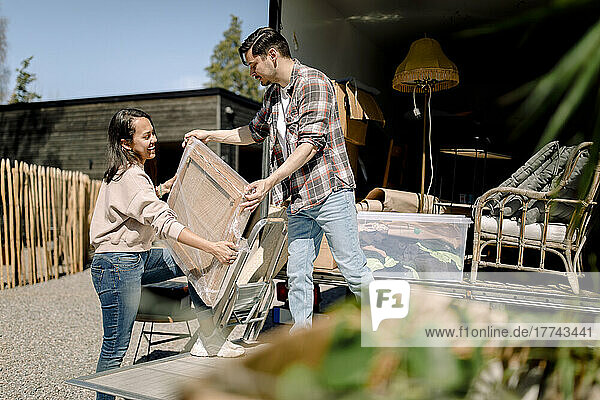 Mann und Frau beim Entladen von Gemälden aus einem Lastwagen an einem sonnigen Tag