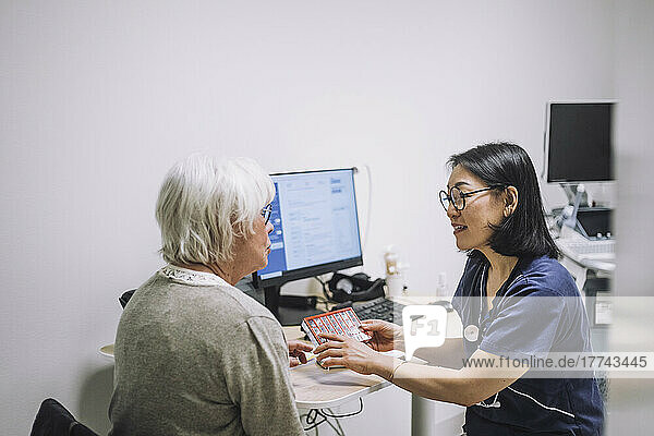 Reife Ärztin diskutiert mit älterem Patienten im Krankenhaus über Pillenorganisator