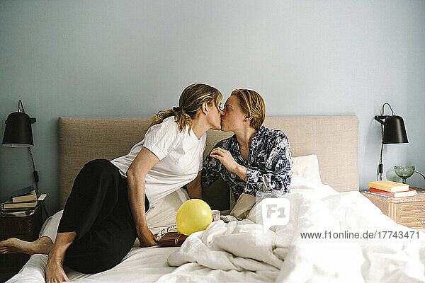 Lesbische Frau mit Geburtstagsgeschenk küsst Freundin auf dem Bett zu Hause