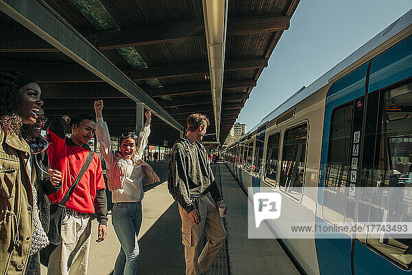 Happy multiracial friends cheering up on arrival of train at railroad station