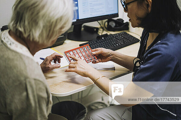 Female doctor discussing over pill organizer with senior patient sitting at desk in office