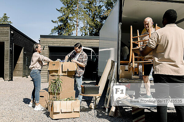 Professionelle Umzugshelfer tragen Stühle vom Lastwagen  während ein Paar Kisten durchsucht