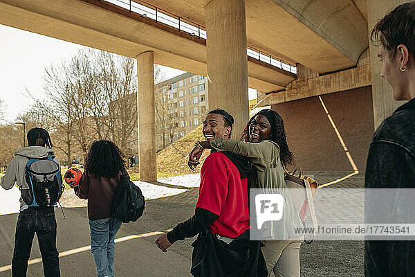 Seitenansicht von fröhlichen multirassischen Freunden  die gemeinsam unter einer Brücke spazieren gehen