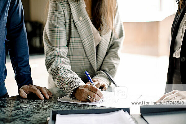 Midsection of couple signing contract with real estate agent in kitchen