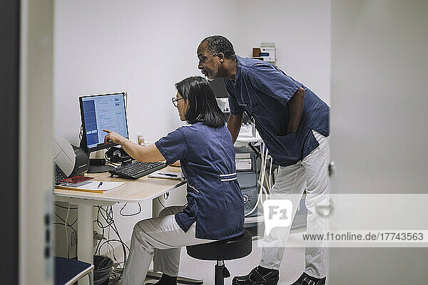 Eine Ärztin zeigt auf einen Computerbildschirm  während sie mit einem männlichen Kollegen im Krankenhaus diskutiert