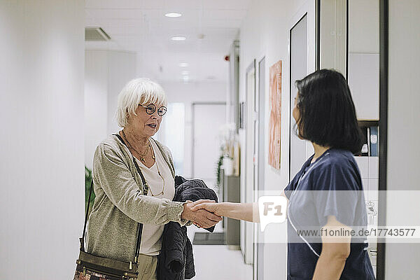 Lächelnde ältere Frau schüttelt Hände mit einer Ärztin  die an der Tür eines Krankenhauses steht