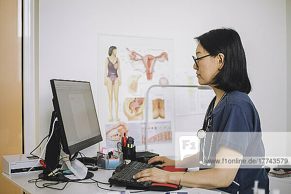 Side view of female healthcare expert using computer sitting at desk in hospital