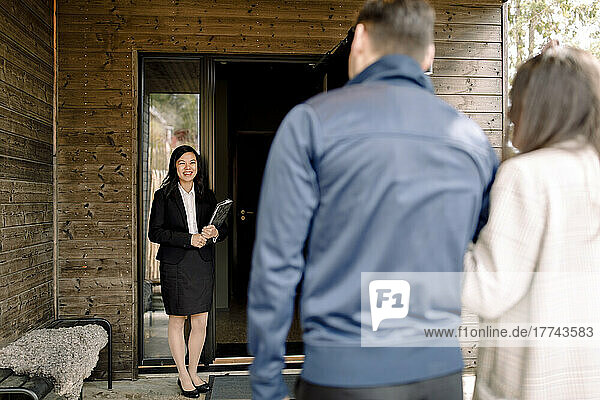 Smiling real estate agent greeting couple at entrance of house