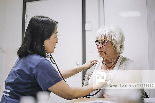 Mitarbeiterin des Gesundheitswesens untersucht älteren Patienten mit Stethoskop in einer medizinischen Klinik