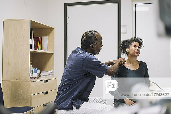 Male healthcare worker examining shoulder female patient grimacing with pain in medical clinic