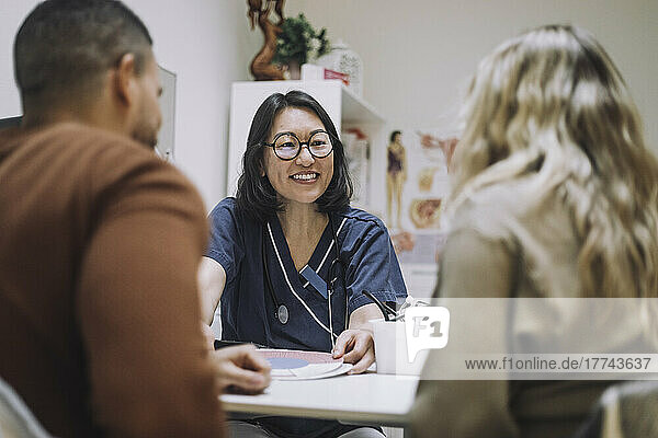 Happy female healthcare expert discussing over chart with couple in medical clinic