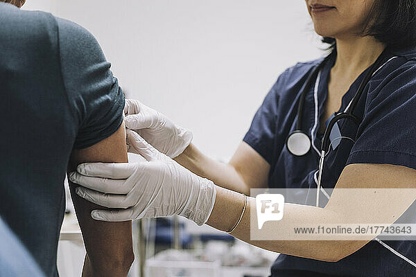 Midsection of female gynecologist wearing protective gloves examining patient in medical clinic