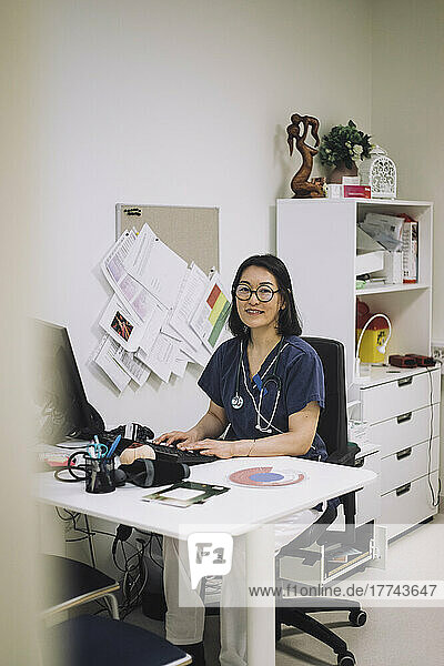 Porträt einer lächelnden Ärztin  die am Schreibtisch in einer medizinischen Klinik sitzt