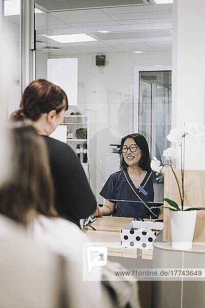 Lächelnde Empfangsdame  die Patienten an der Kasse in einer medizinischen Klinik hilft