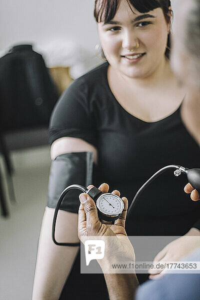 Lächelnde weibliche Patientin  die einen männlichen Arzt bei der Blutdruckmessung in einer medizinischen Klinik ansieht