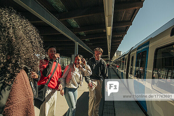 Multirassische spielerische Freunde stehen in der Nähe des Zuges am Bahnhof