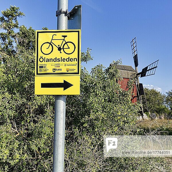 Gelbes Verkehrsschild  Wegweiser mit Piktogramm Fahrrad für schwedischen Radwanderweg Ölandsleden  dahinter Windmühle  Insel Öland  Kalmar län  Schweden  Europa