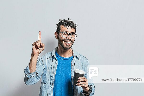 Junger Mann mit Papier Kaffeebecher zeigt Finger nach oben  Happy lächelnde Person mit Papier Kaffeebecher zeigt Finger nach oben