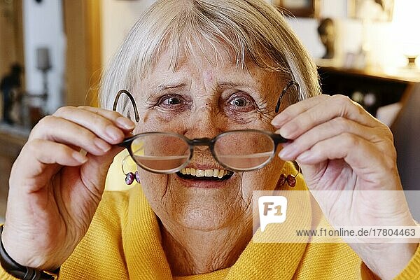 Senior woman puts on her glasses smiling at home  Bocholt  North Rhine-Westphalia  Germany  Europe