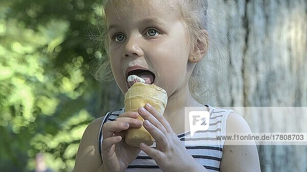 Süßes kleines Mädchen isst draußen Eis. Close-up-Porträt von blonden Mädchen sitzen auf Parkbank und essen Eis. Odessa  Ukraine  Europa