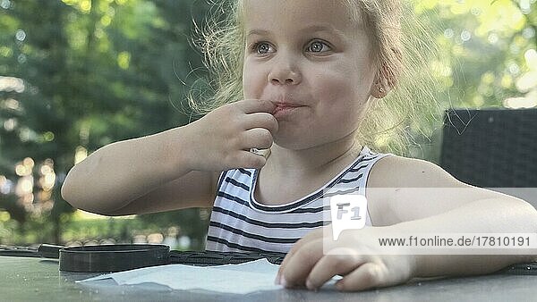 Kleines Mädchen schmeckt Salz. Close-up-Porträt von blonden Mädchen nimmt Salz aus Serviette mit dem Finger und schmeckt es  während in Straßencafé auf dem Park sitzen. Odessa Ukraine