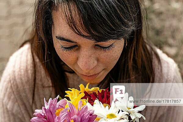 Blick von oben auf eine junge Frau  die an einem Strauß Gänseblümchen in ihren Händen riecht. Nahaufnahme