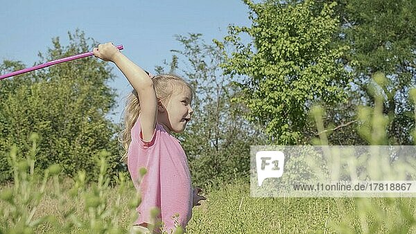 Kleines Mädchen spielt mit Schmetterlingsnetz von hohem Gras im Stadtpark. Nettes kleines Mädchen spielt mit Luftinsektennetz in Wiese auf Sonne Tag. Odessa  Ukraine  Europa